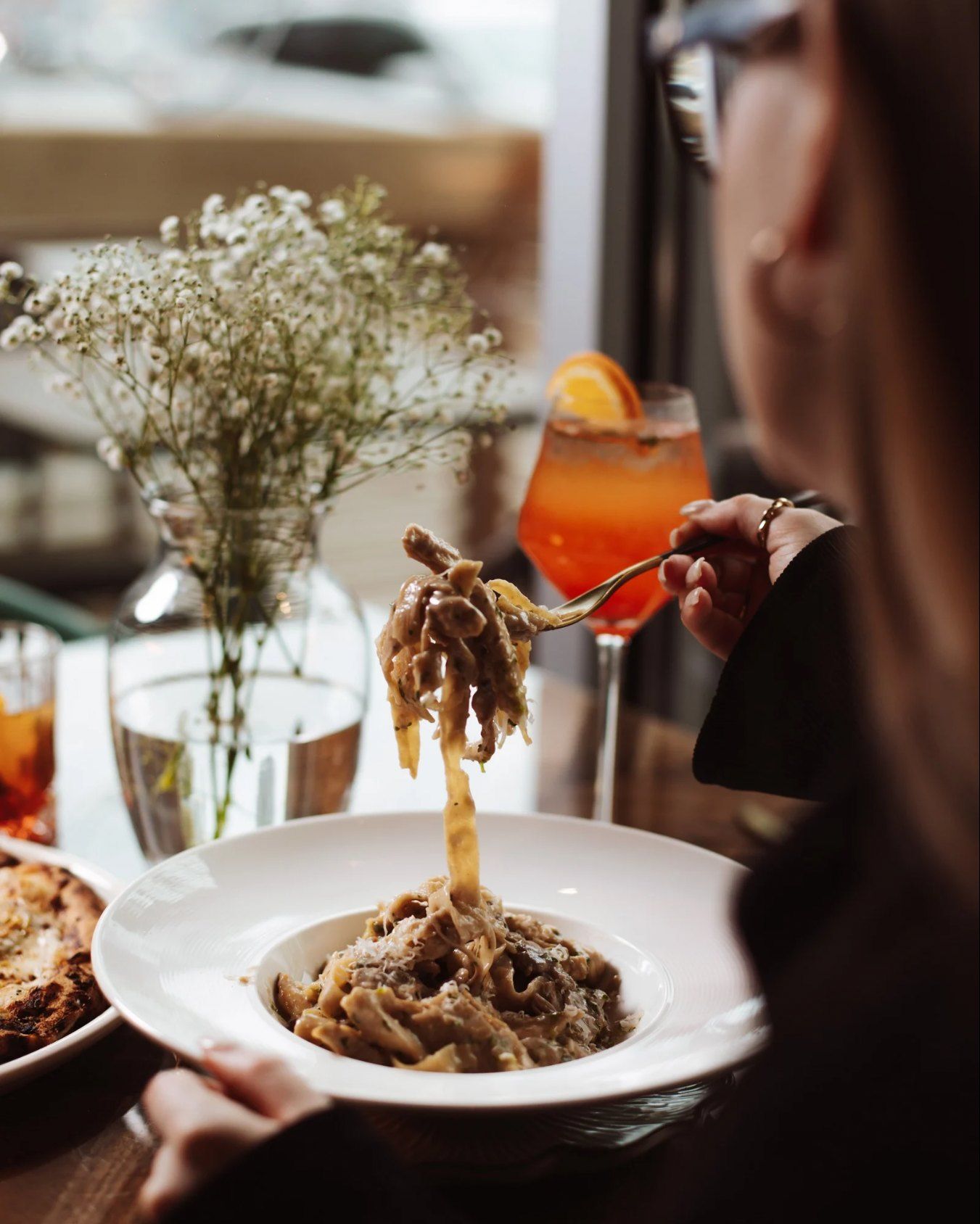 A guest twirling house-made tagliatelle, with a spritz on the table