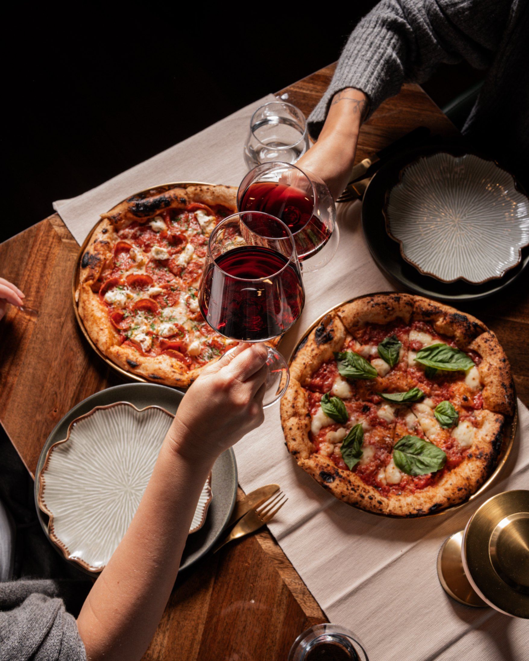 Guests toasting with red wine over pepperoni and margherita pizzas